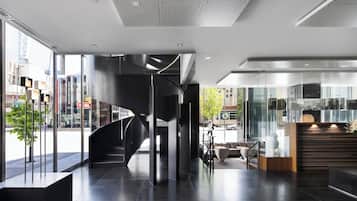 Un interior moderno con una escalera espiral, un mostrador de recepción y grandes ventanales que dan a la calle.