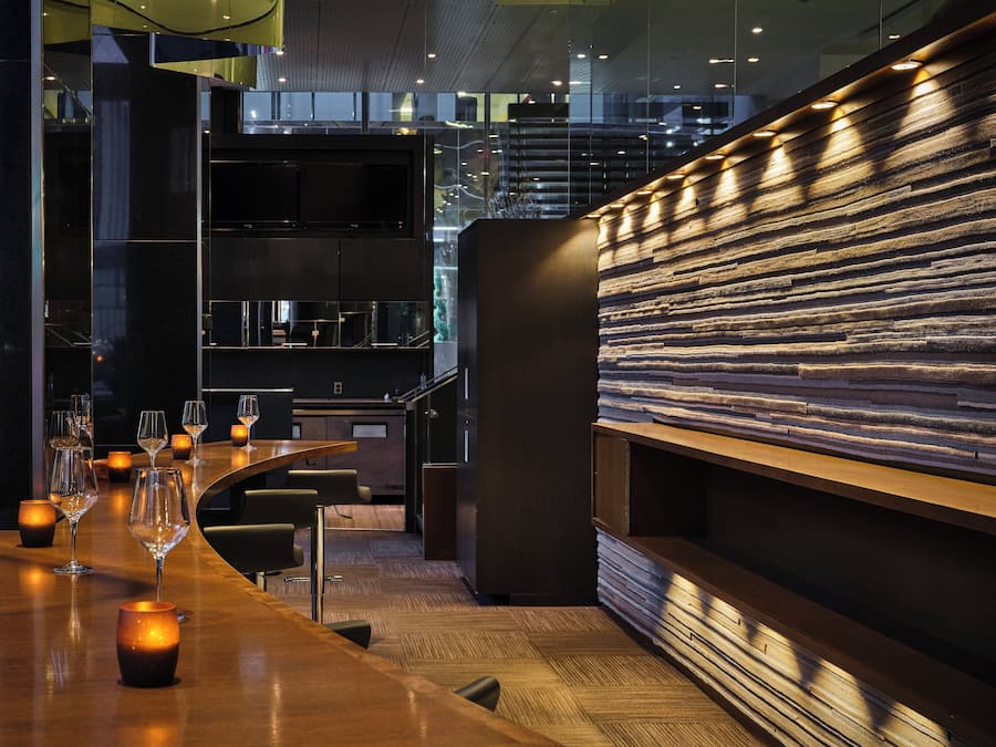 A modern bar area with a curved wooden counter, multiple glasses, and candles.