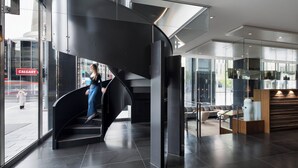 A modern interior with a curved staircase, glass walls, and a seating area with a wooden accent wall. - Hotel Le Germain Calgary (Calgary)