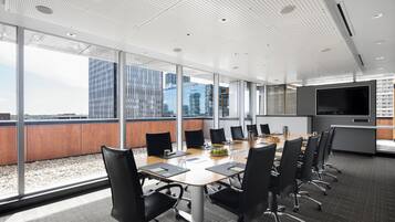 Uma sala de conferência moderna com uma grande mesa, cadeiras pretas e um ecrã grande.