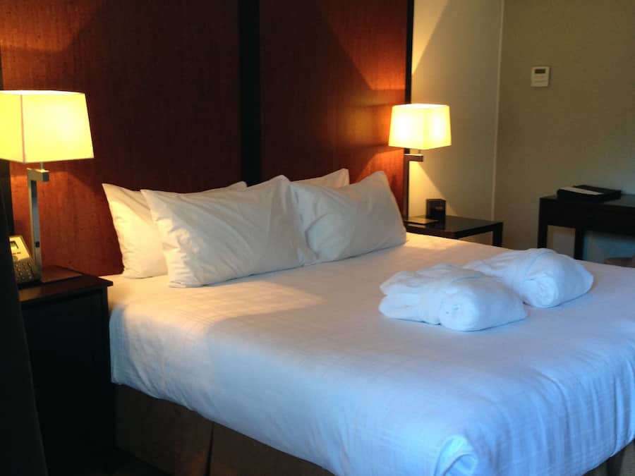 A hotel room with a large bed, two bedside lamps, a wooden headboard, and a small table with a phone.