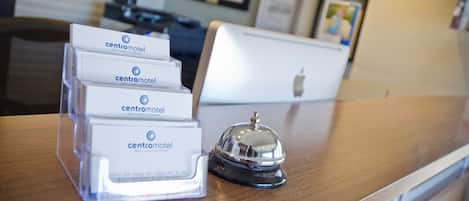 A hotel reception desk with a clear plastic sign holder displaying multiple 'Centromotel' signs, a silver bell, and a laptop computer.