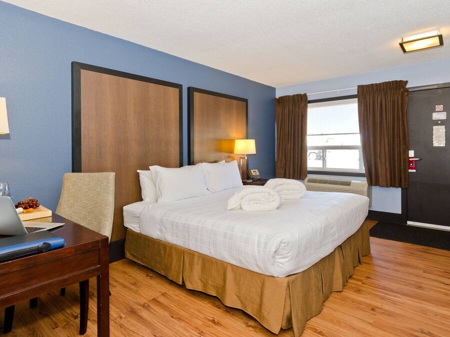 Habitación de hotel con cama, escritorio, laptop, lámpara y ventana con cortinas.