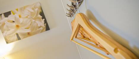 A wall-mounted wooden rack with multiple hooks, a framed picture of white flowers, and a light fixture.
