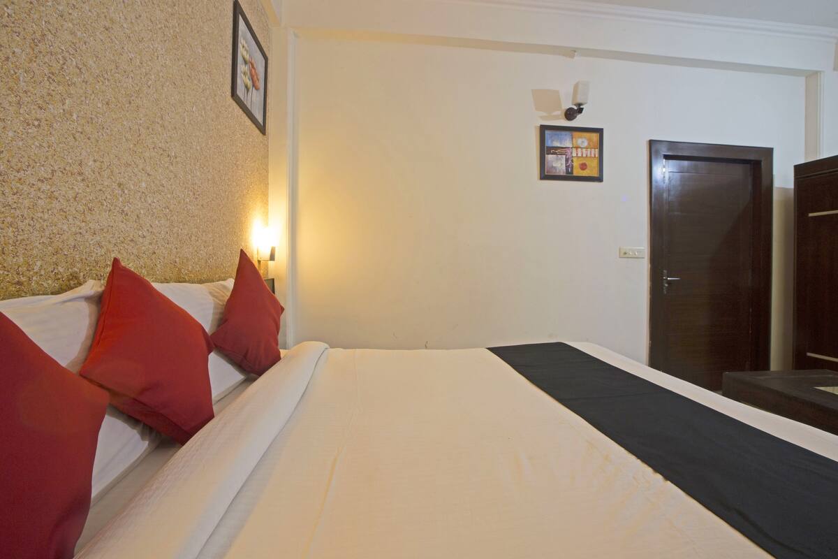 A hotel room with a bed, pillows, a wall-mounted light, a door, and a small picture frame.