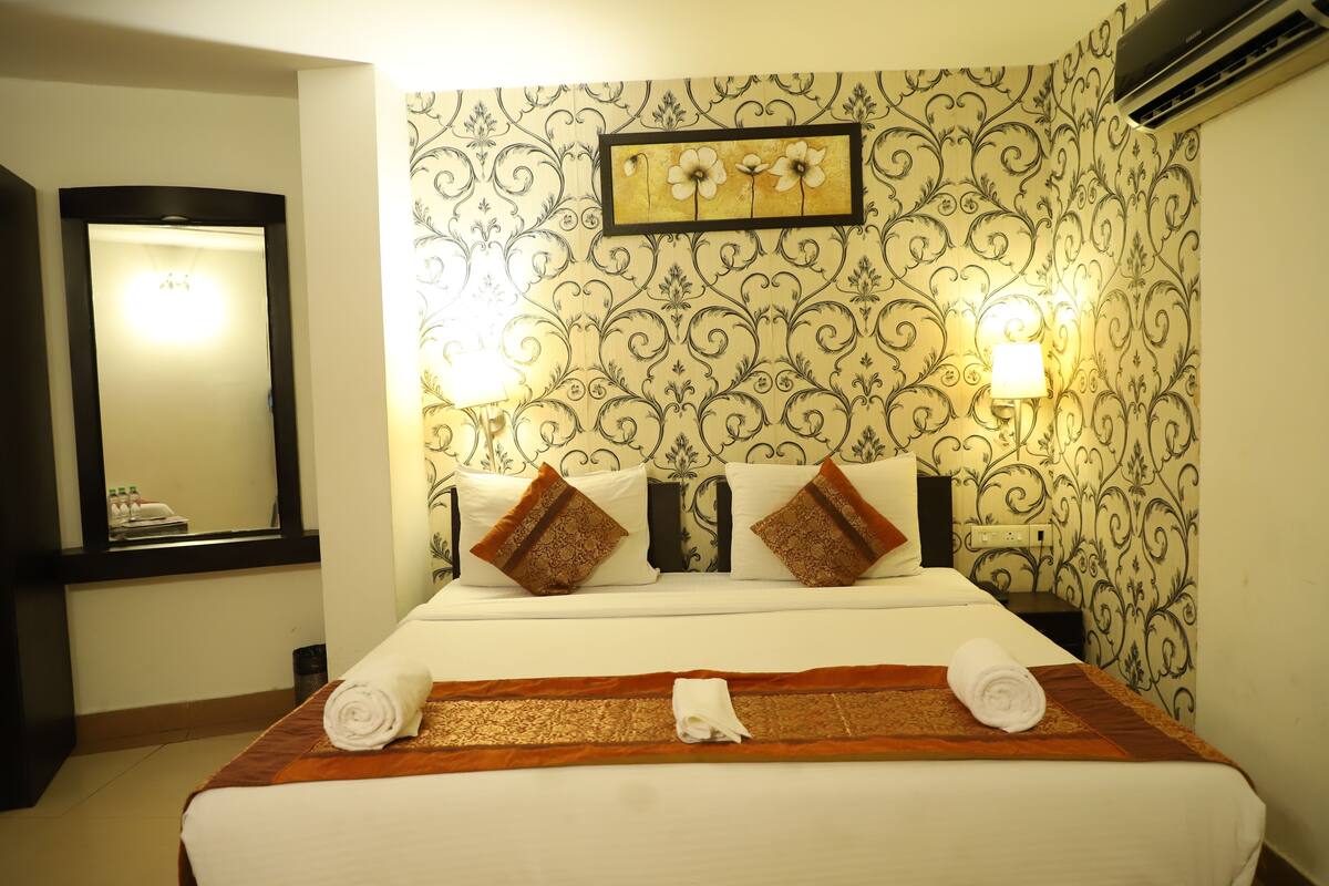A neatly made bed with a patterned headboard, two wall-mounted lamps, and a framed floral artwork above the bed.