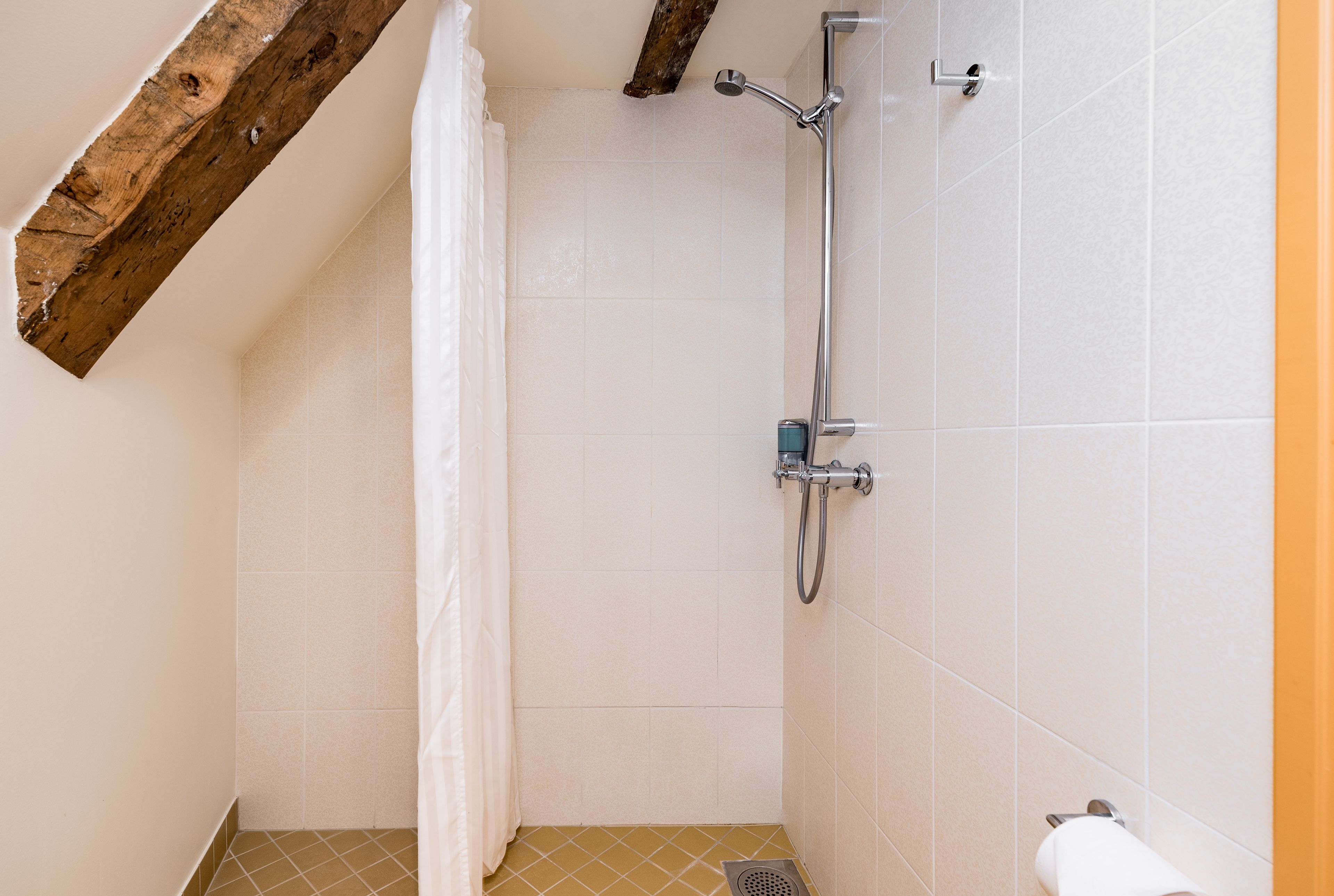Een douche met een houten balk, witte tegels en een metalen douchekop.