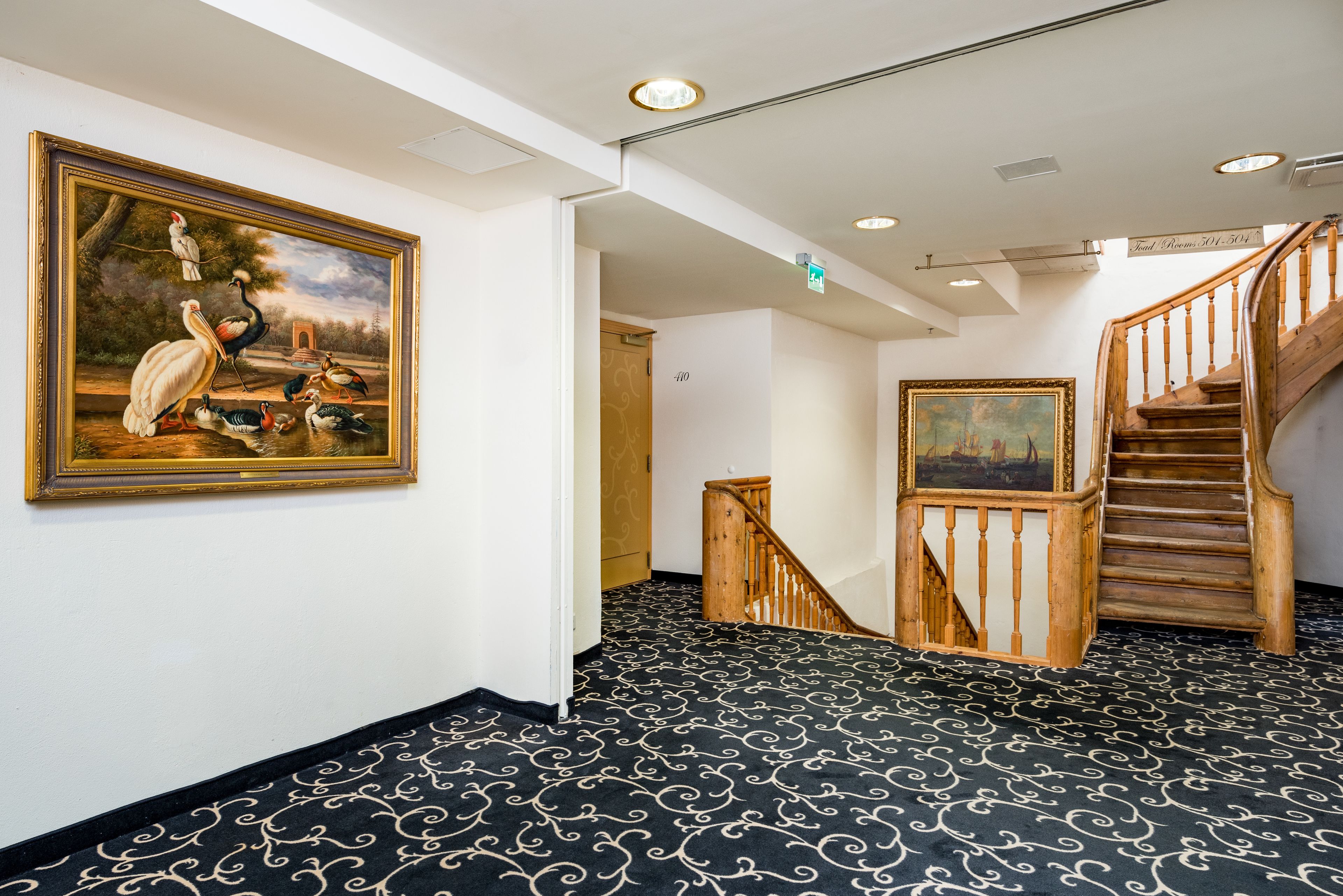 Un couloir avec un tapis à motifs noir et blanc, un escalier en bois et deux tableaux encadrés accrochés aux murs.