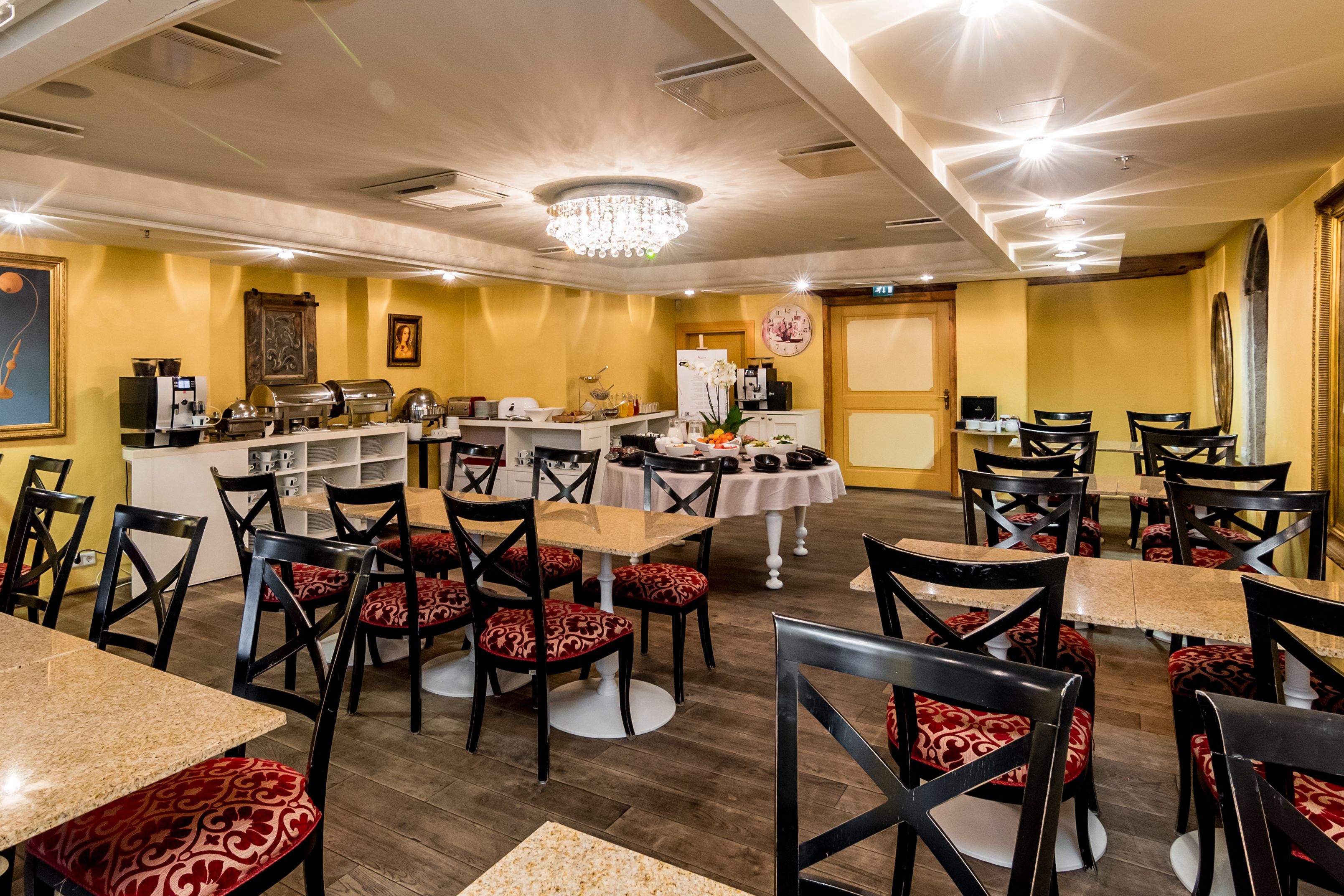 A restaurant with multiple tables and chairs, a counter with food and drink stations, and a chandelier.