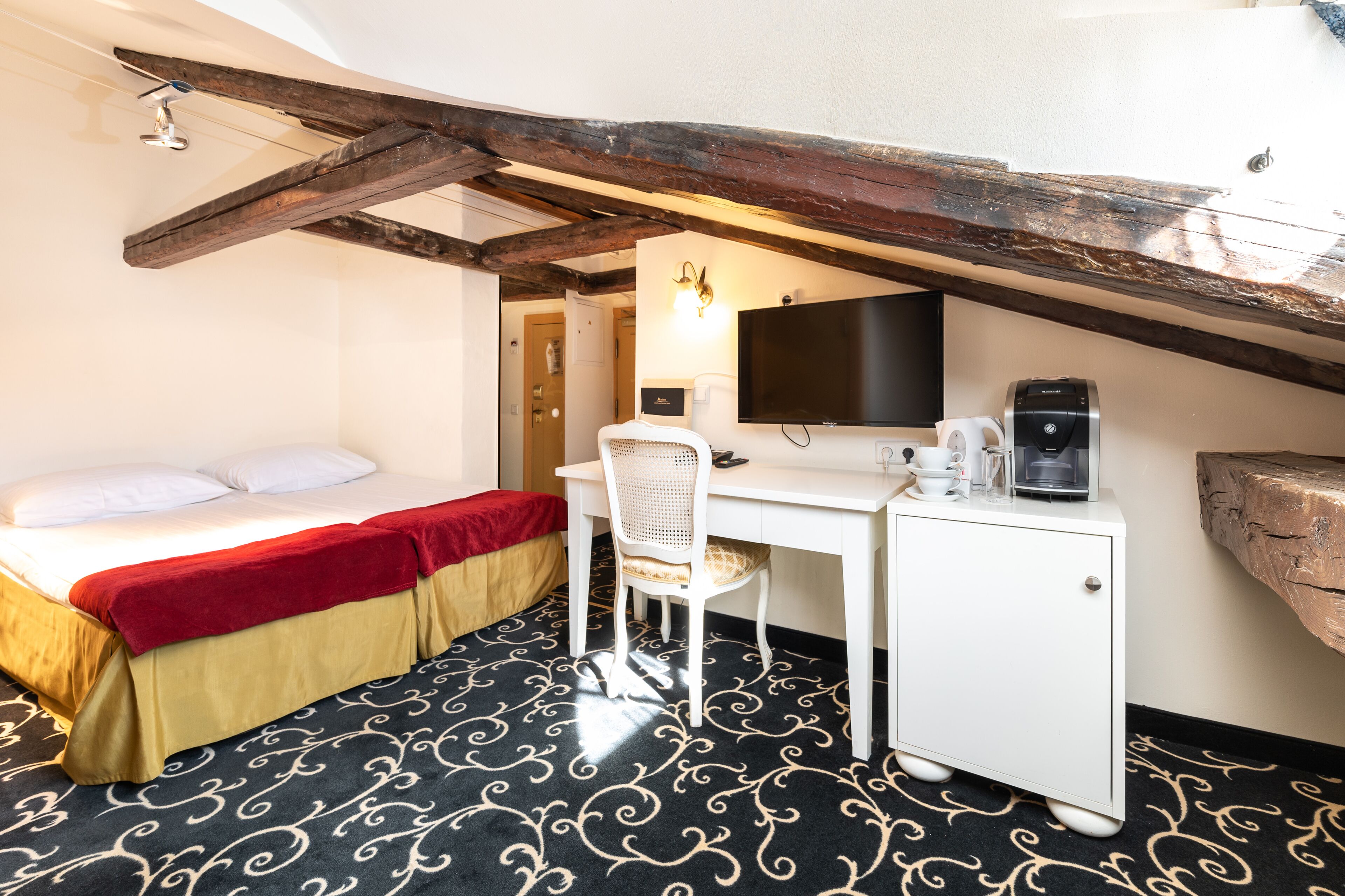 A hotel room with a bed, desk, chair, and a television.