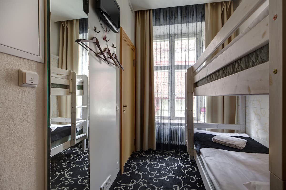 Una habitación de hotel con literas, un espejo, un radiador y una ventana con cortinas.