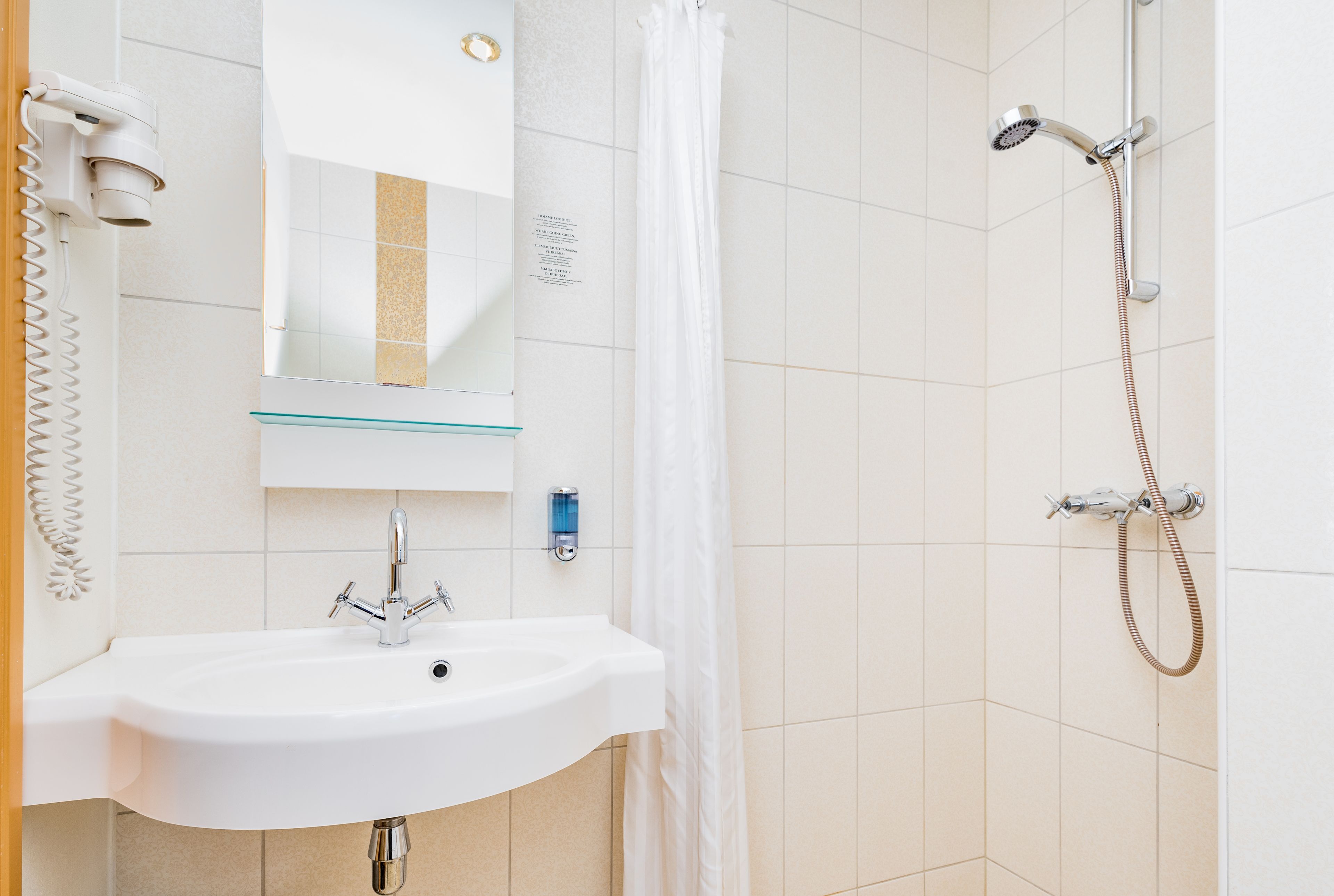 Ein Badezimmer mit weißem Waschbecken, Spiegel, Dusche mit Duschbrause und Handtuchhalter.