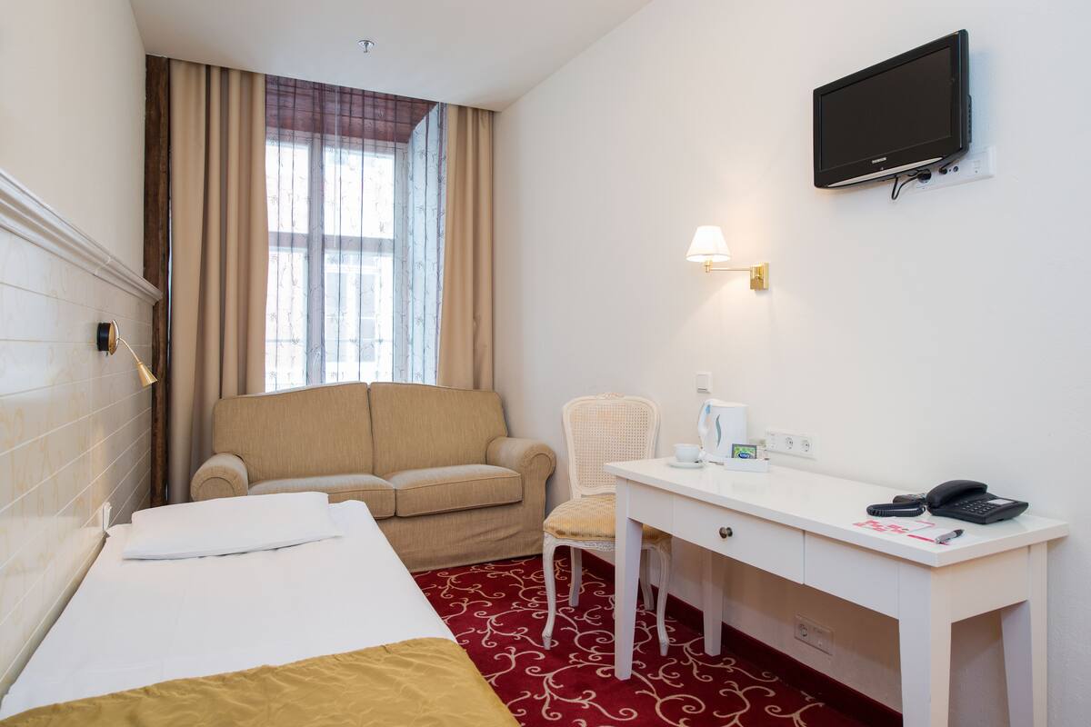 Una habitación de hotel con cama, escritorio, silla, televisor y ventana con cortinas.
