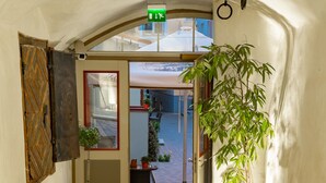Un portail en arc donnant sur une rue, avec un pot de fleurs sur la droite et une porte ornée d’un motif géométrique sur la gauche.