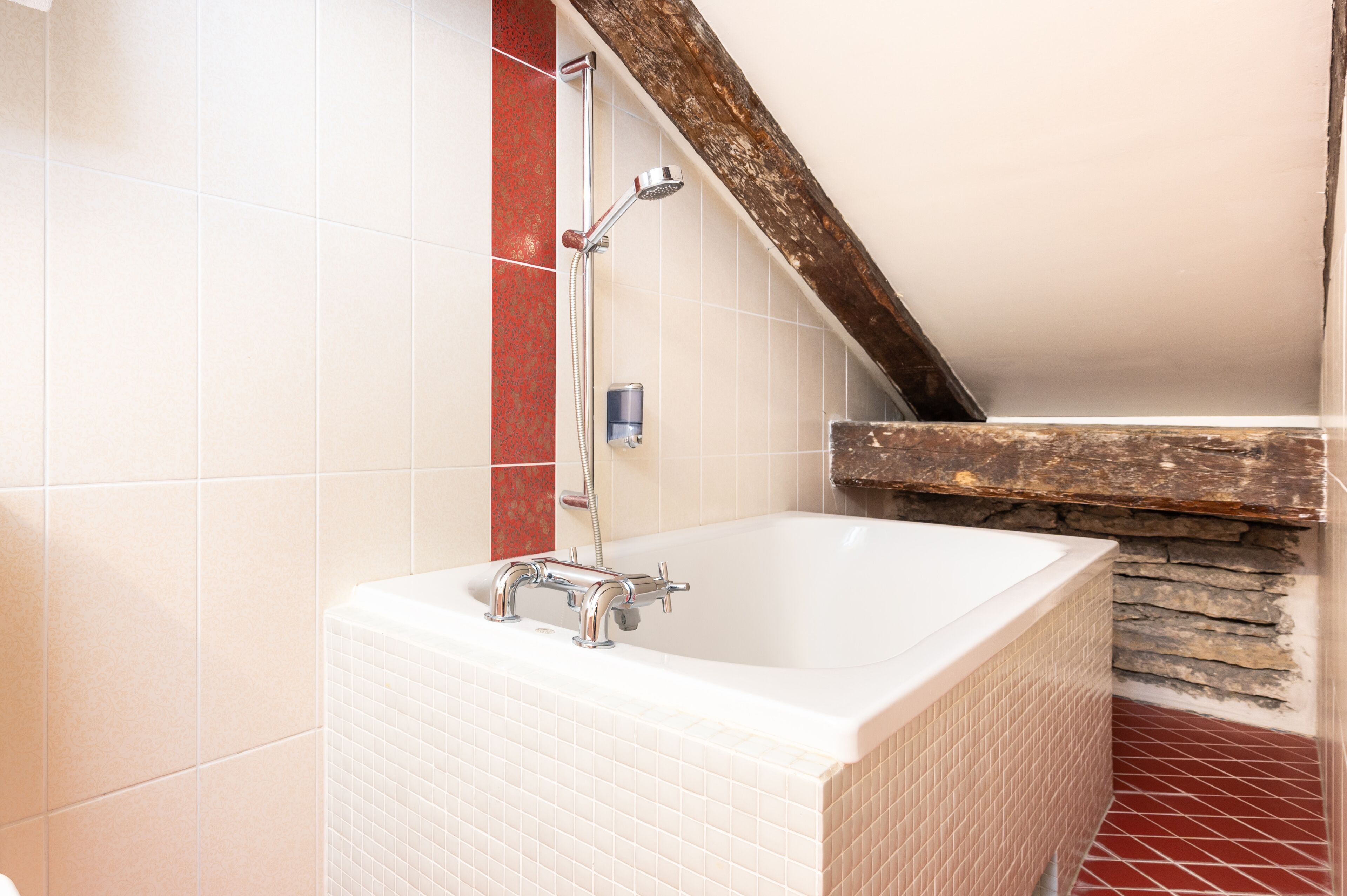 A bathroom with a white bathtub, a showerhead, and a red-tiled wall.
