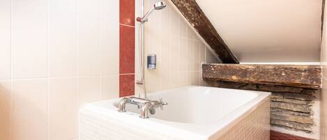 A bathroom with a white bathtub, a showerhead, and a red-tiled wall.