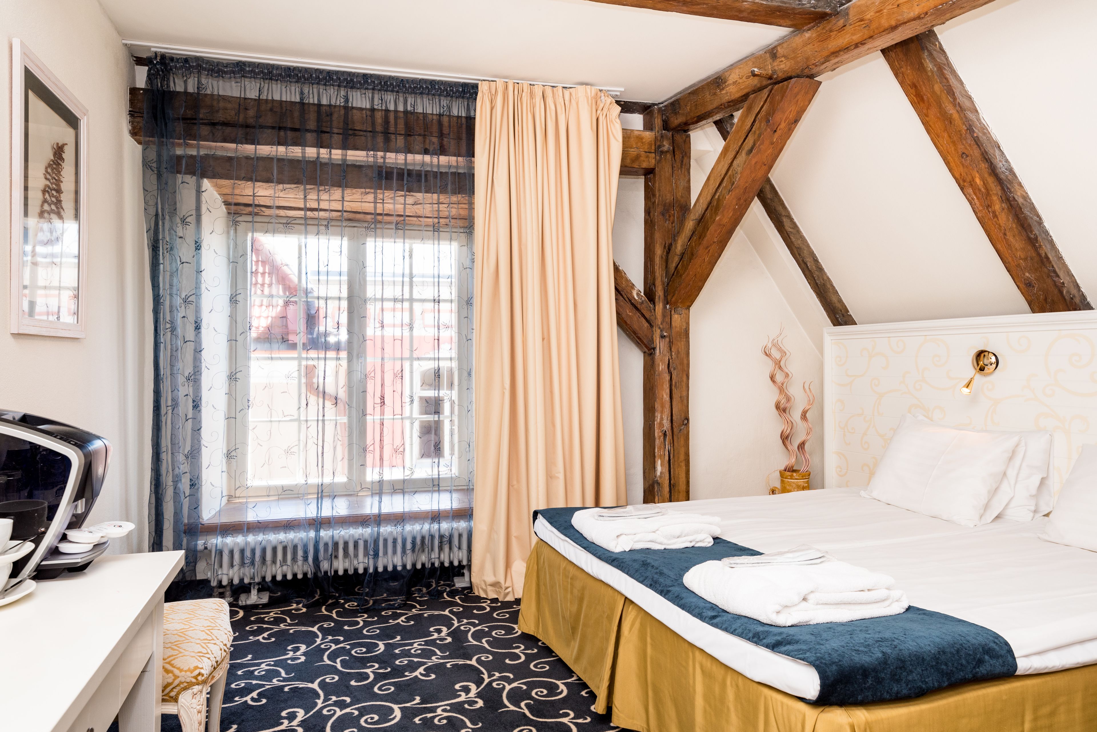 A hotel room with a bed, a desk, a radiator, and a window with curtains.