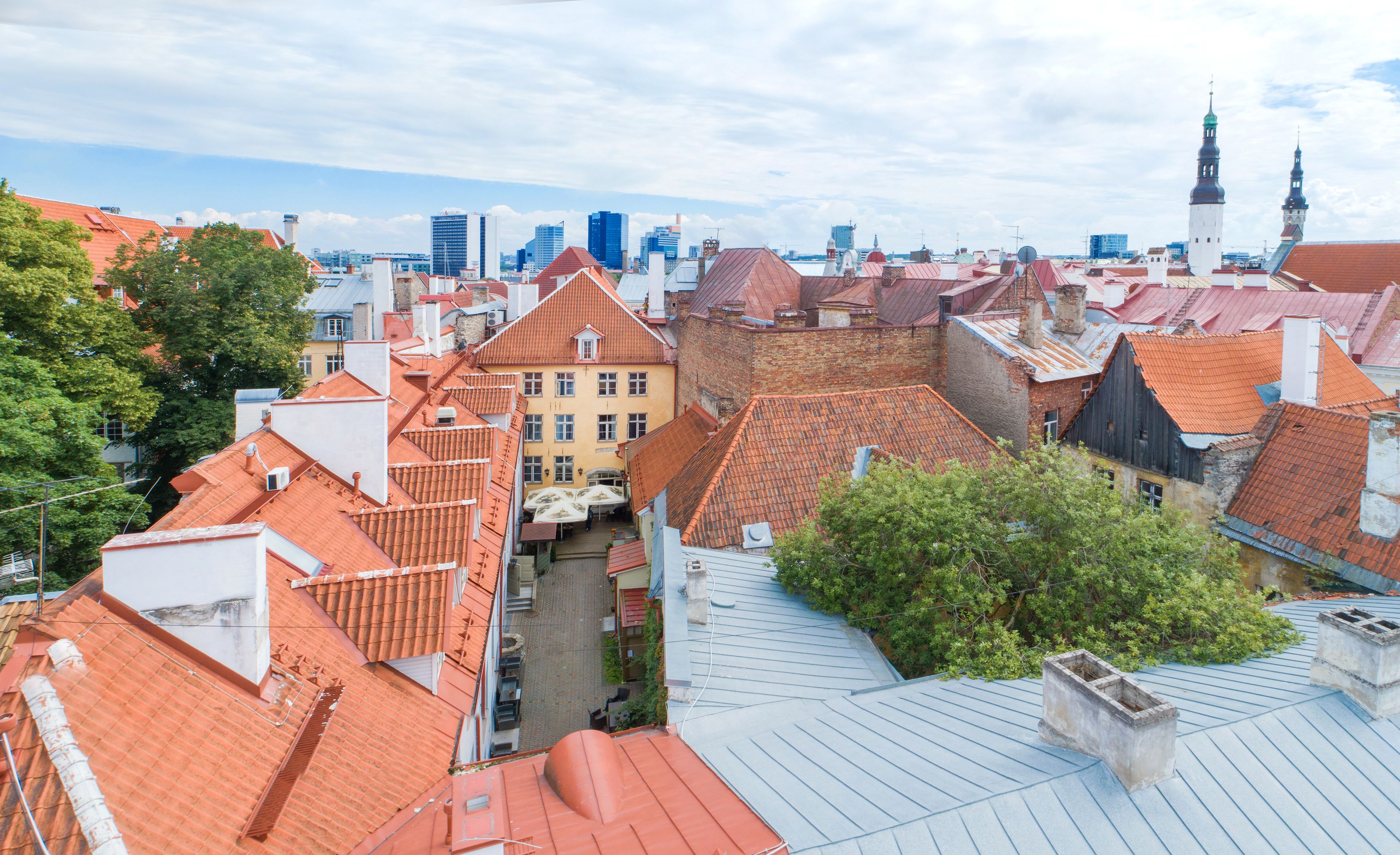 A high-angle view of a cityscape with red-tiled rooftops, historic buildings, and modern skyscrapers in the background.