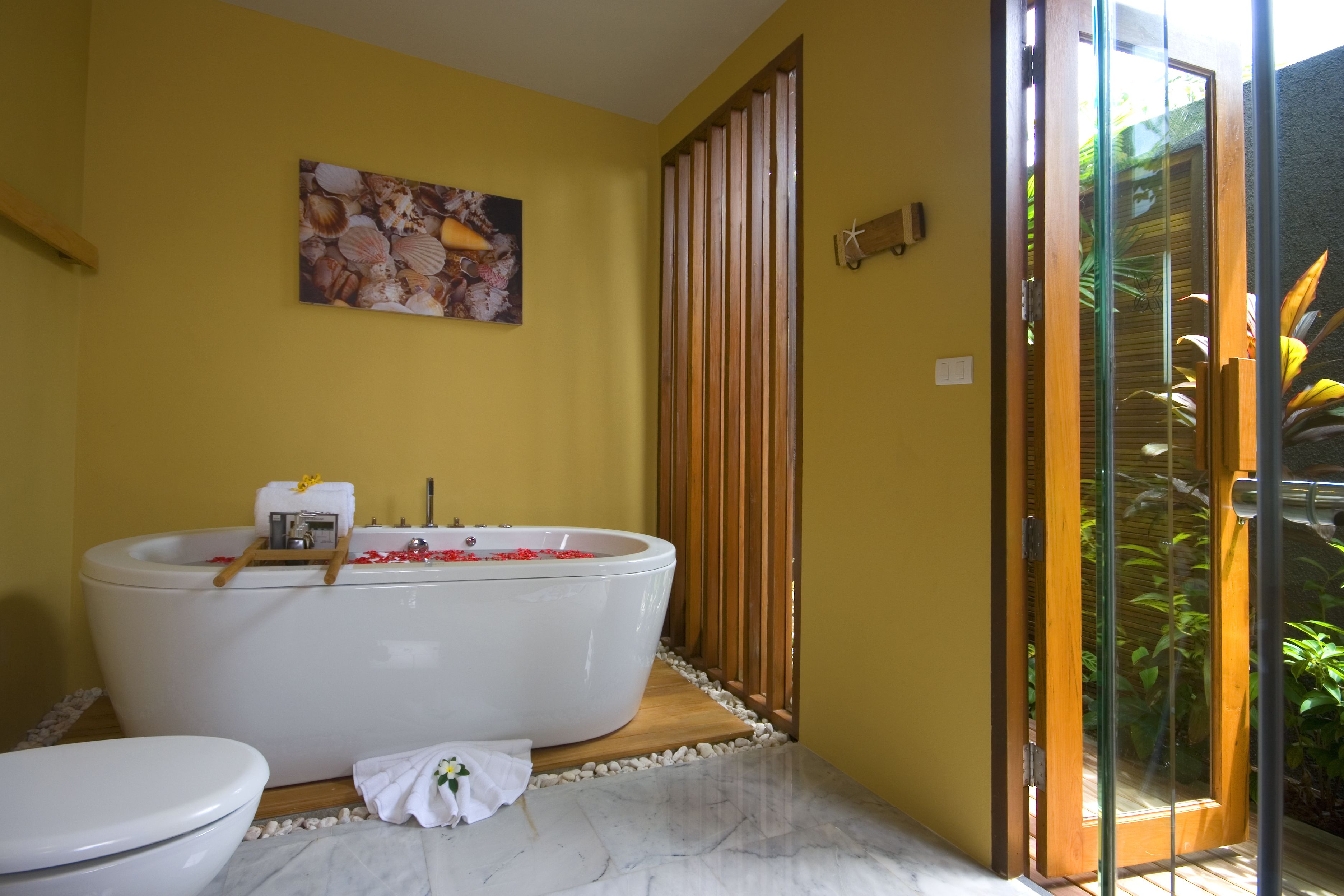 Une salle de bain avec une baignoire sur pieds, des toilettes et une porte en verre donnant sur un jardin.
