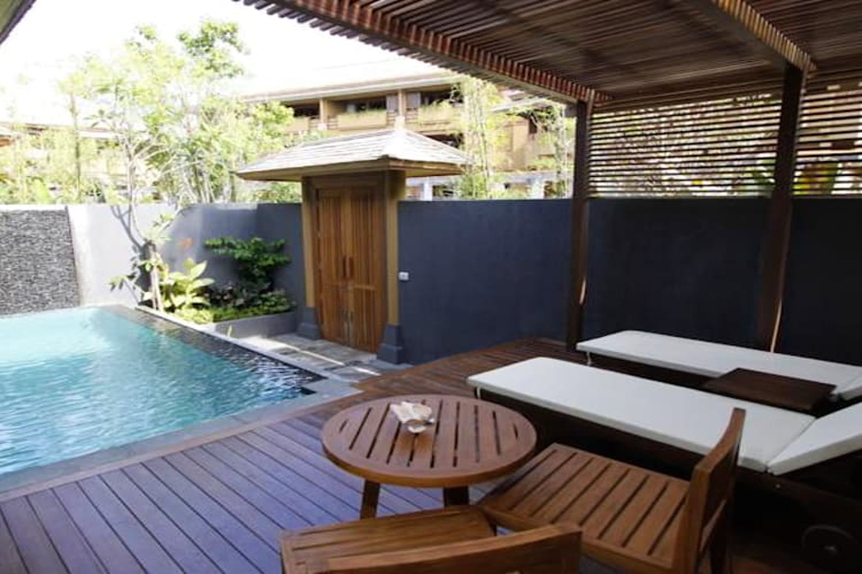 A pool area with wooden deck, lounge chairs, and a small table.