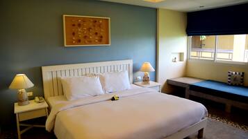 Habitación de hotel impecable con una cama grande, lámparas de noche, una mesita pequeña y un banco junto a la ventana.