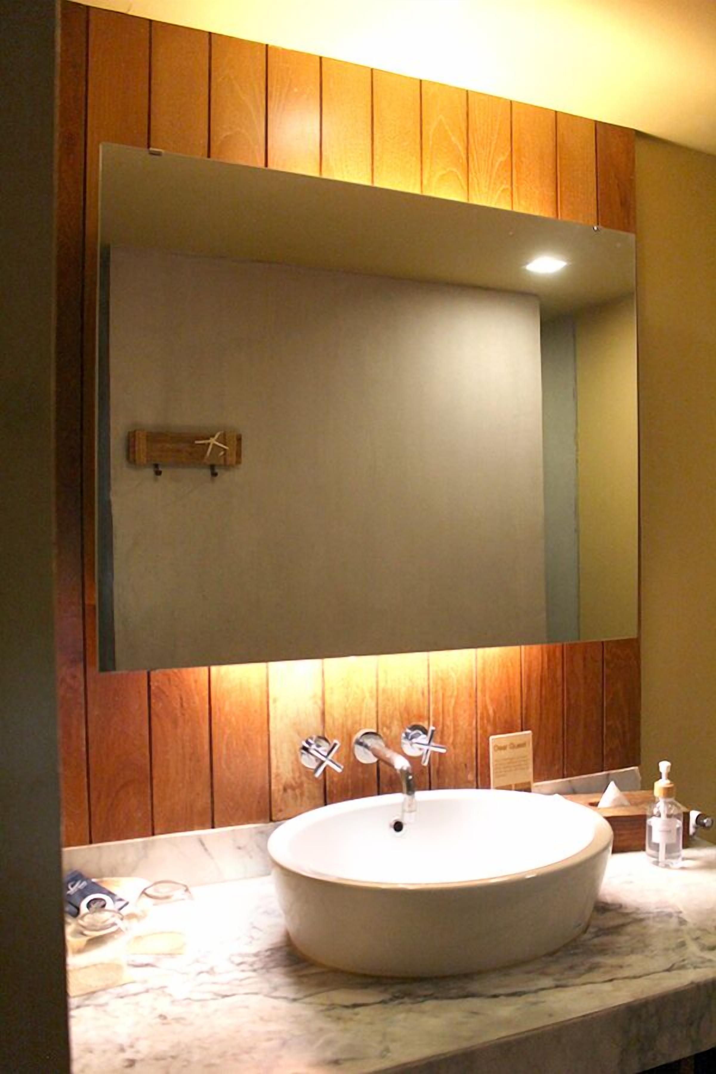 Un baño con un espejo grande, paneles de madera, un lavamanos redondo y una encimera de mármol.