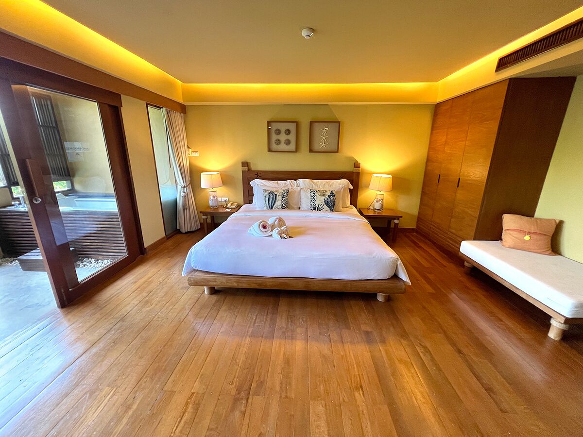 A hotel room with a large bed, bedside lamps, a wooden floor, and a sliding door leading to a balcony.