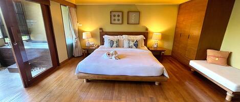 Una habitación de hotel con una cama grande, lámparas de noche, suelo de madera y una puerta corredera que da a un balcón.