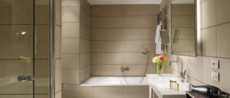 A modern bathroom with a glass shower enclosure, a bathtub, a sink with toiletries, and a mirror.