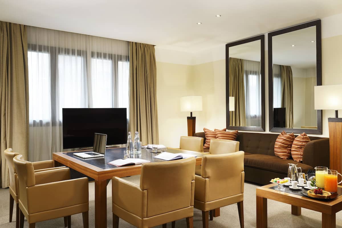 A hotel room with a dining table, chairs, a sofa, a TV, and a breakfast setup.