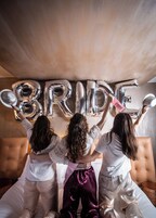Three people standing in front of a wall with the word "BRIDE" spelled out in silver balloons.