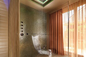 A modern bathroom with a glass shower enclosure, a textured wall, and a large window with curtains.