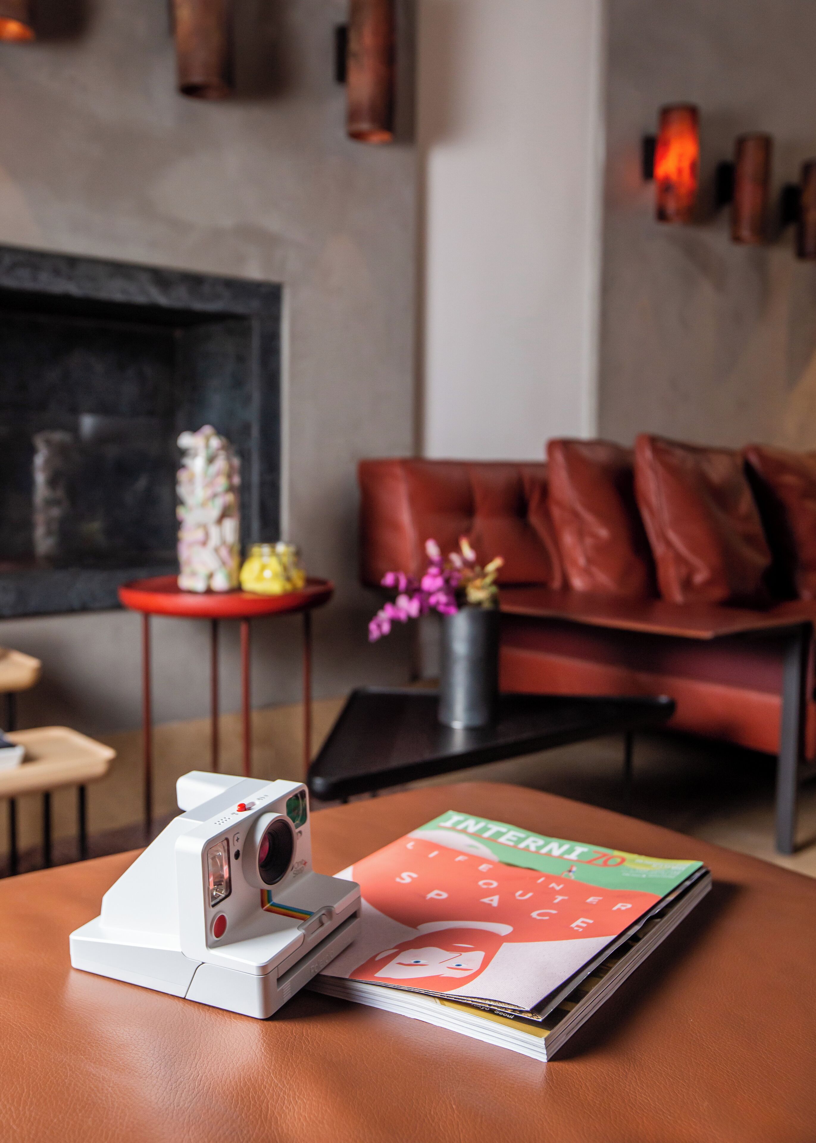 A modern living room with a leather sofa, a small table with a camera, and a magazine.