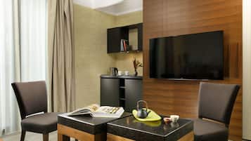 Een moderne hotelkamer met een flatscreen televisie, een houten kast met boeken, een klein tafeltje met een tijdschrift, een theepot en twee stoelen.