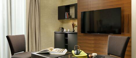 Una camera d'albergo moderna con una televisione a schermo piatto, un mobiletto in legno con dei libri, un tavolino con una rivista, un bollitore e due sedie.
