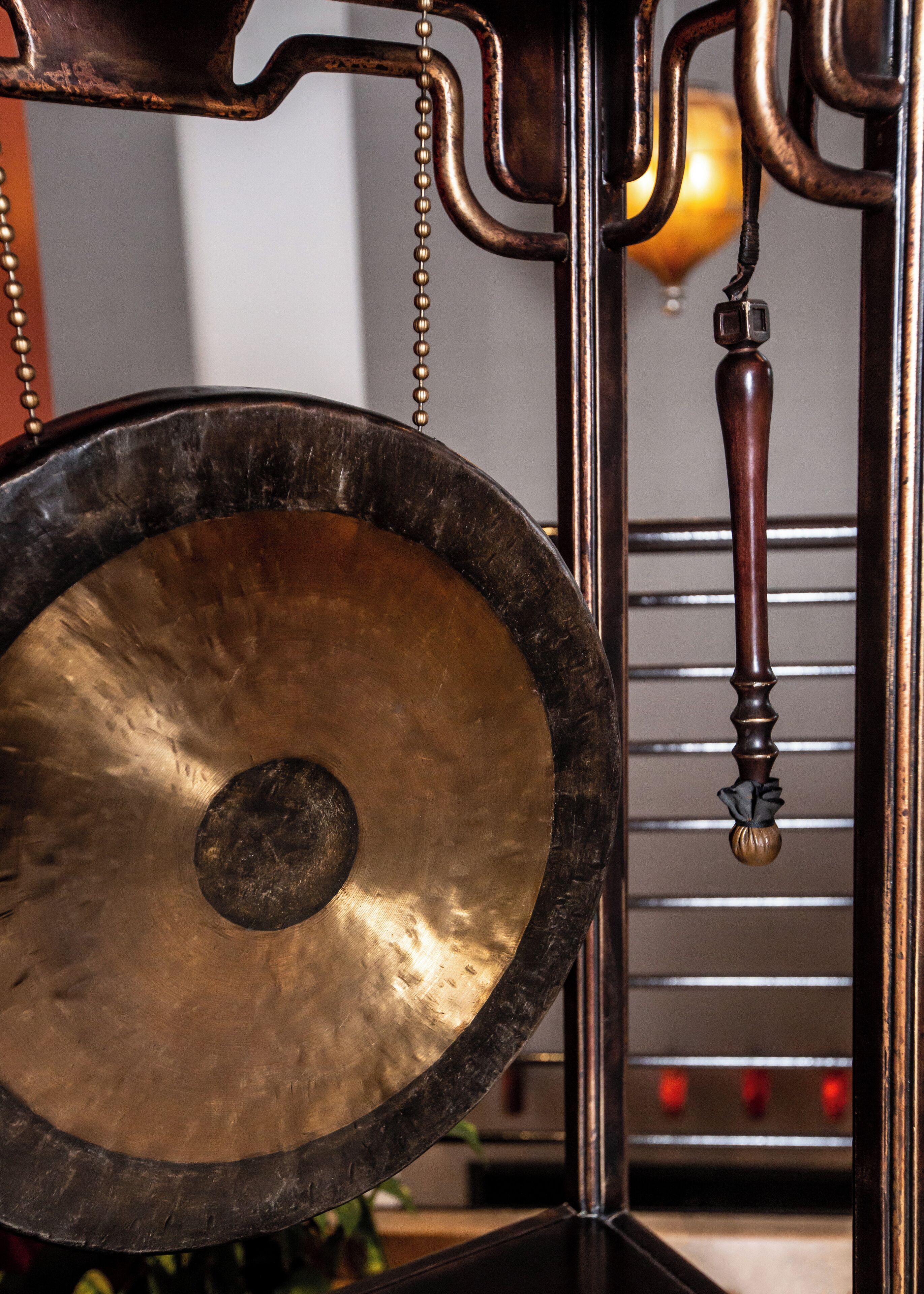 A brass gong with a wooden handle hanging from a metal structure.