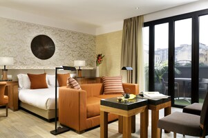 A hotel room with a bed, sofa, coffee table, and a view of the city through large windows.