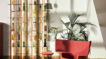 A modern interior with a glass shelving unit displaying various decorative items, a red upholstered chair, and a large potted plant.