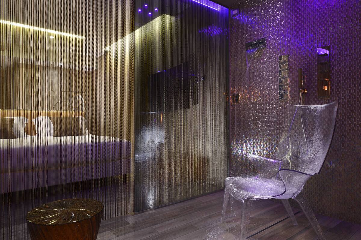 A modern room with a sofa, a clear chair, and a textured wall.