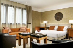A hotel room with a bed, a sofa, a coffee table, and a desk.