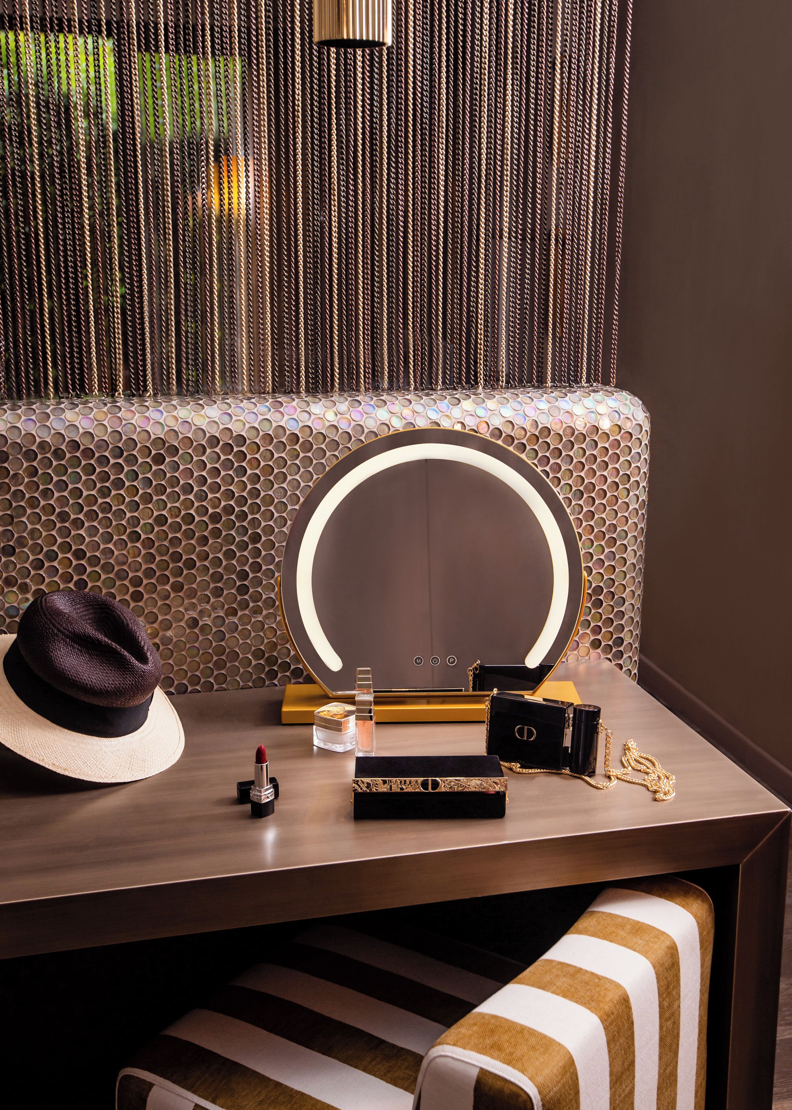 A vanity table with a mirror, makeup, a hat, and a handbag.