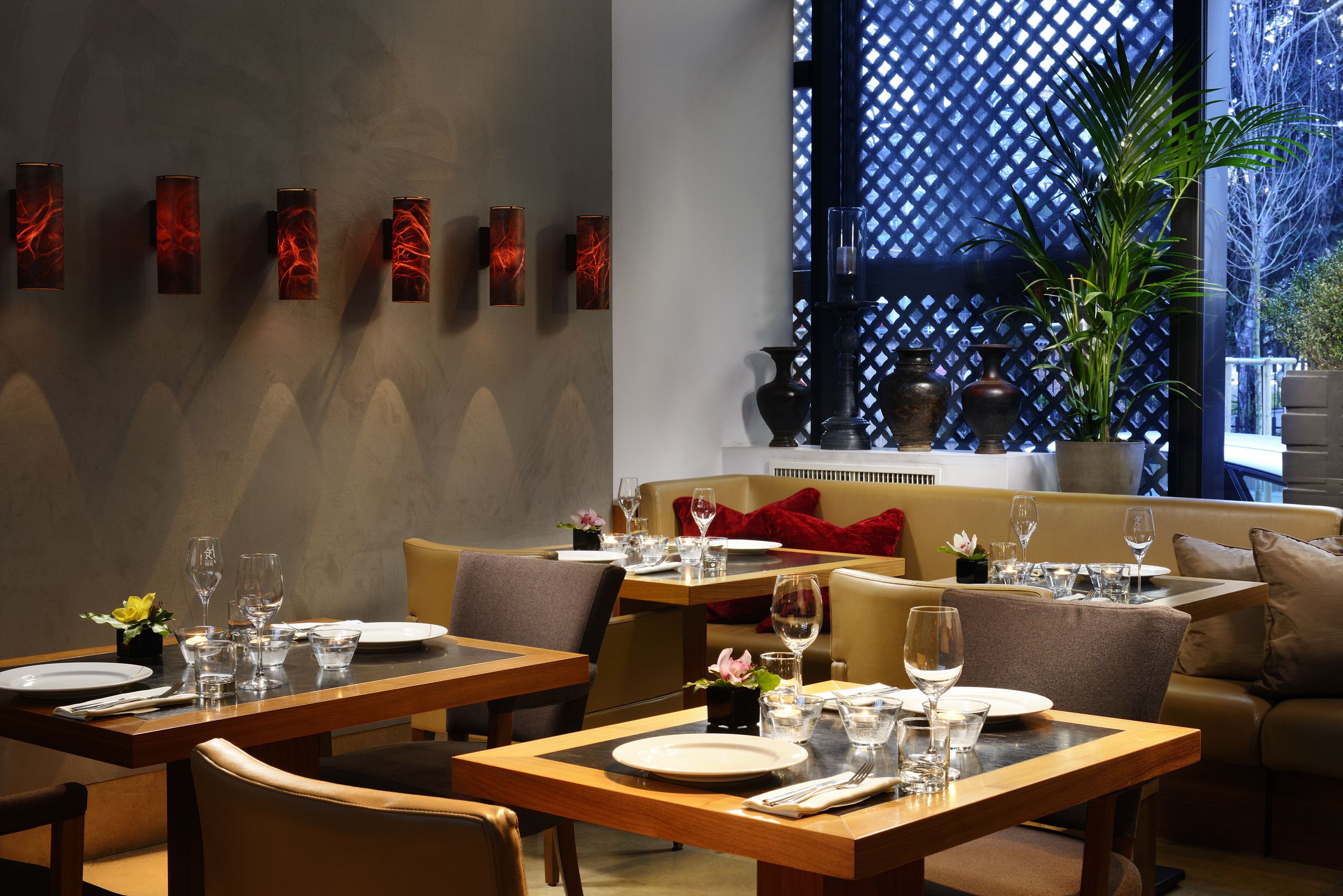 Un coin repas avec des tables préparées pour deux personnes, un canapé et un mur décoratif orné d’œuvres d’art abstraites.