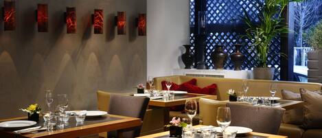 Un comedor con mesas dispuestas para dos, un sofá y una pared decorativa con arte abstracto.