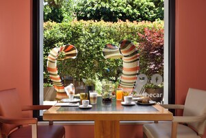 Una tavola imbandita per la colazione, con bevande e dolci, affacciata su un giardino.