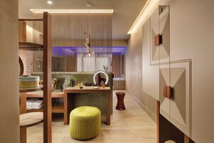 Een moderne badkamer met een houten wastafelmeubel, een ronde gele kruk en een spiegel met verlichting.