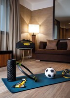 Habitación de hotel con una colchoneta azul para ejercicio, una pesa rusa negra, una pelota de fútbol y una colchoneta de yoga.
