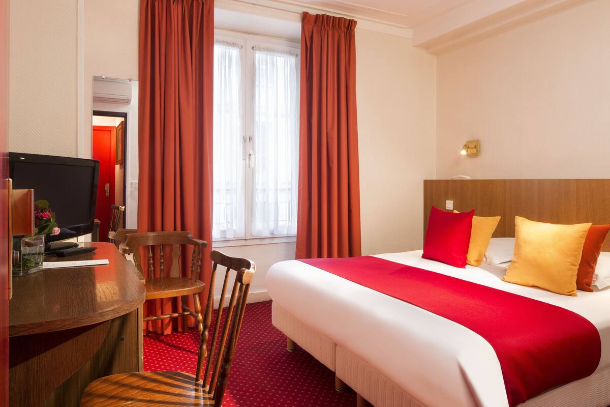 A hotel room with a bed, a desk, a chair, and a television.
