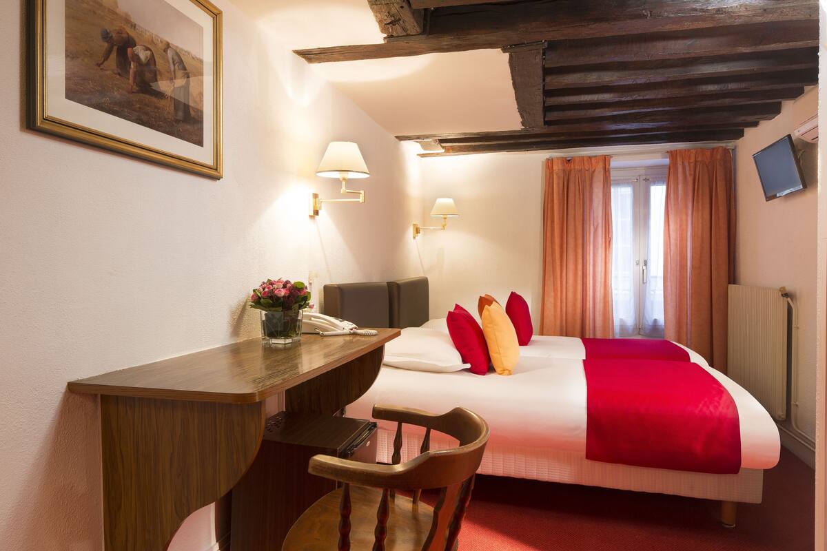 A hotel room with a bed, desk, chair, and a painting on the wall.