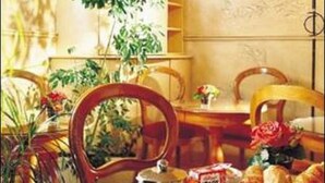 Desayuno con una bandeja que contiene croissants, jugo de naranja y una taza de café, sobre una mesa de madera con sillas.