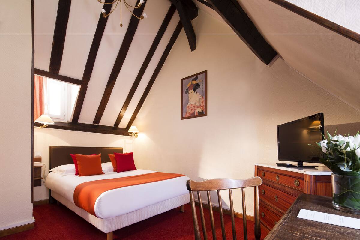 A hotel room with a bed, a television, a wooden chair, and a dresser.